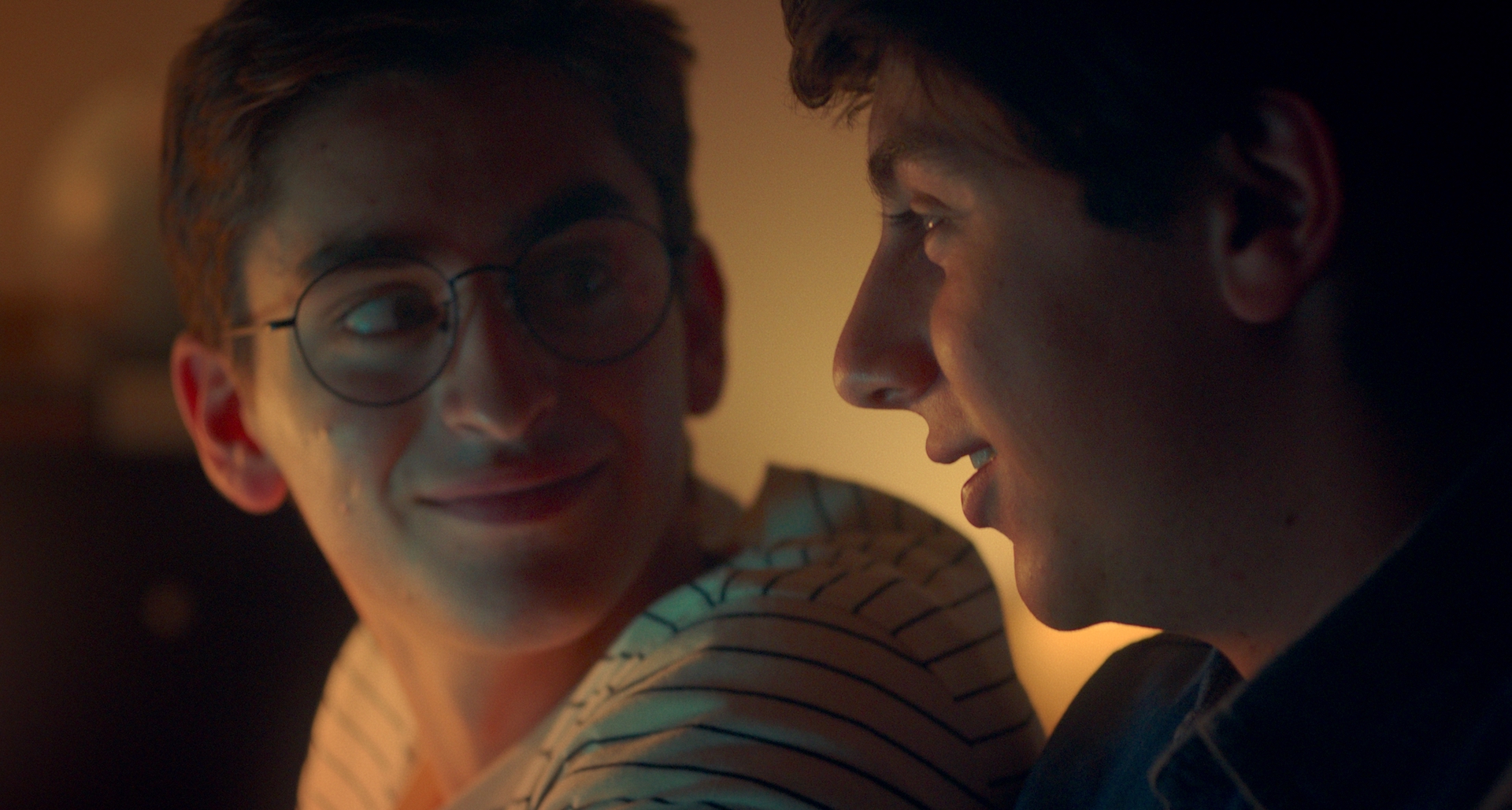 An intimate close up of two teenage boys who are looking at each other, smiling.