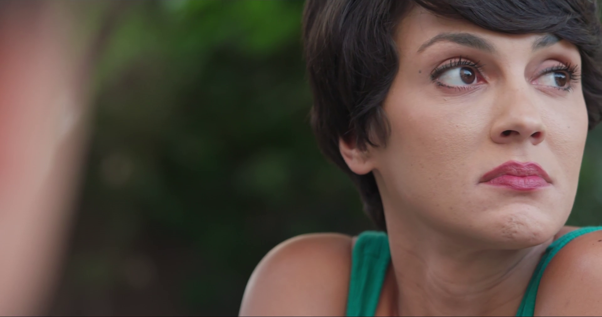 A woman with short hair gazes intently at an unseen object, her expression troubled