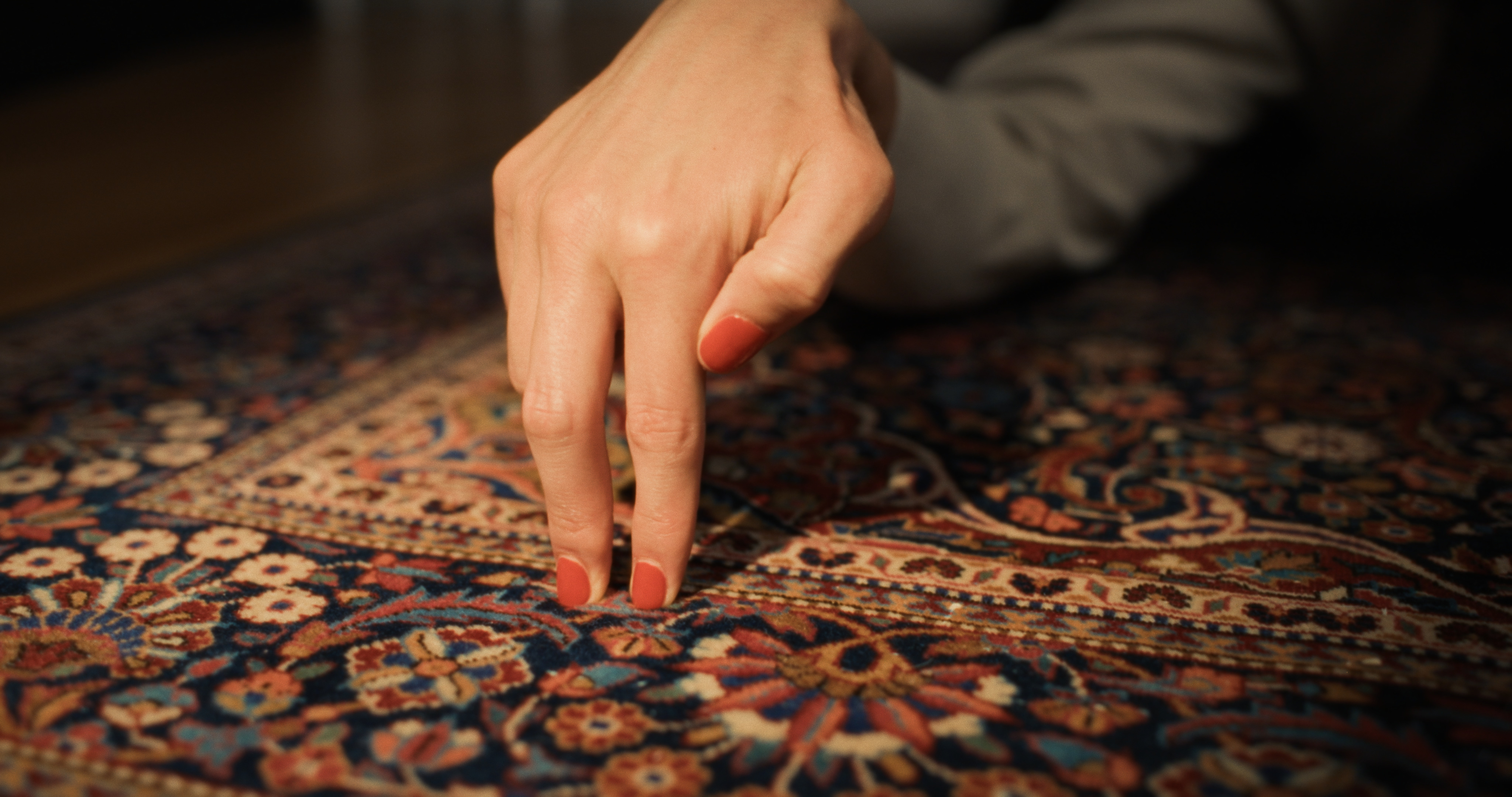 A close up shot from the film “Hand Job” of a hand with nails painted in a standing position on top of a rug.