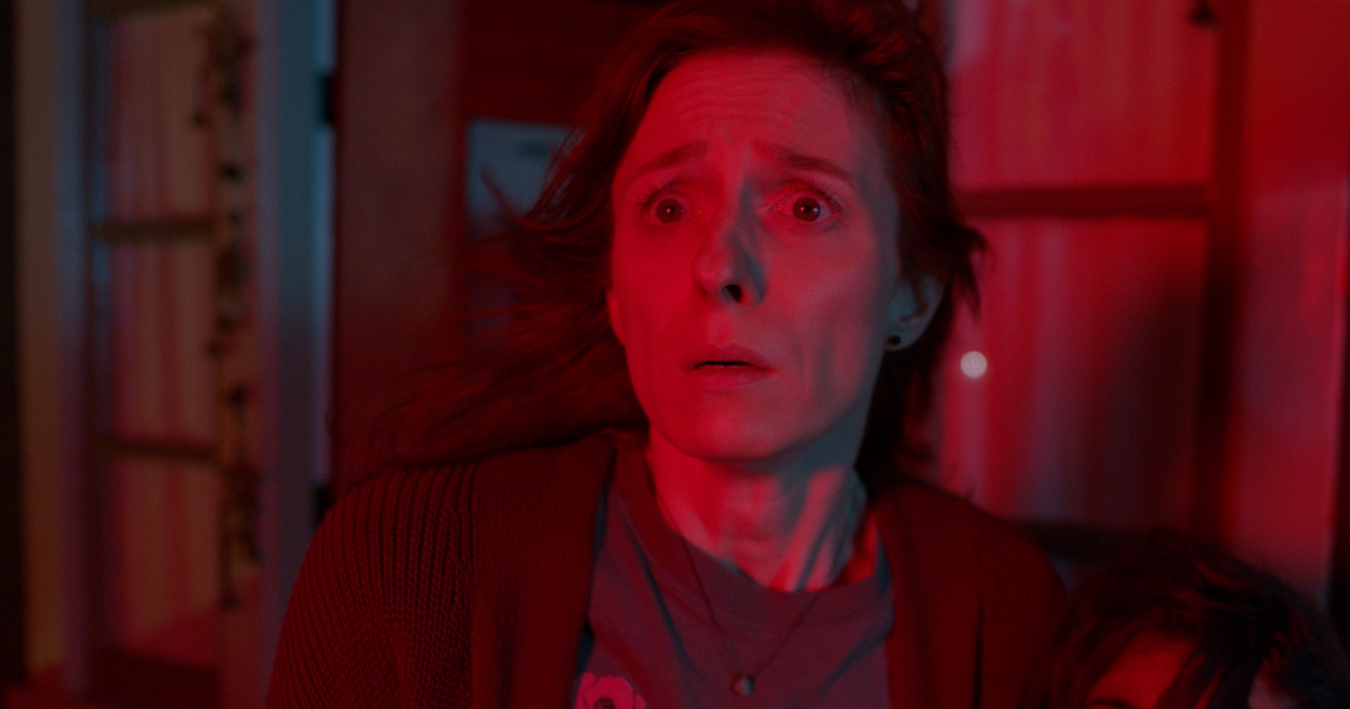 A close up shot from the film “Whitch” of a woman looking at the distance in worry, and a dark red light shines on her.