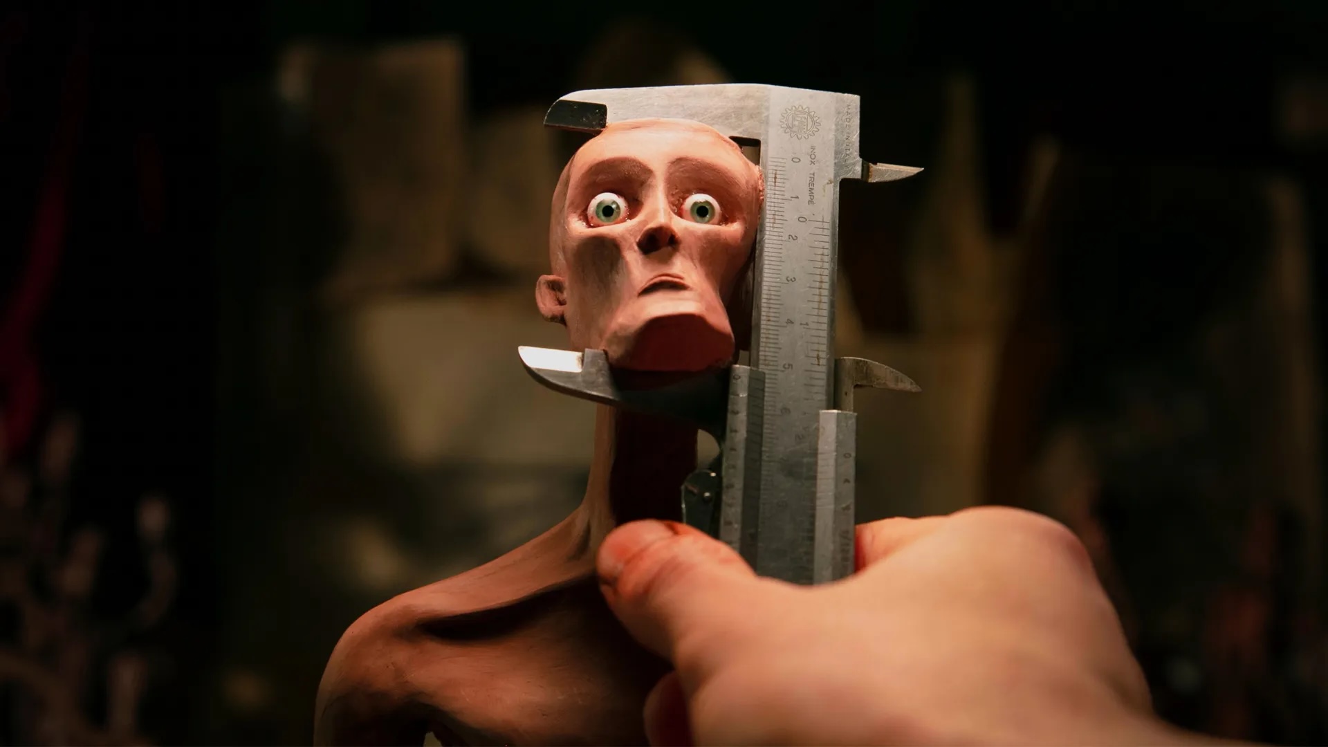 An animated still from the film “Playing God” of a man using a measuring stick on a realistically looking human sculpture to measure their face.