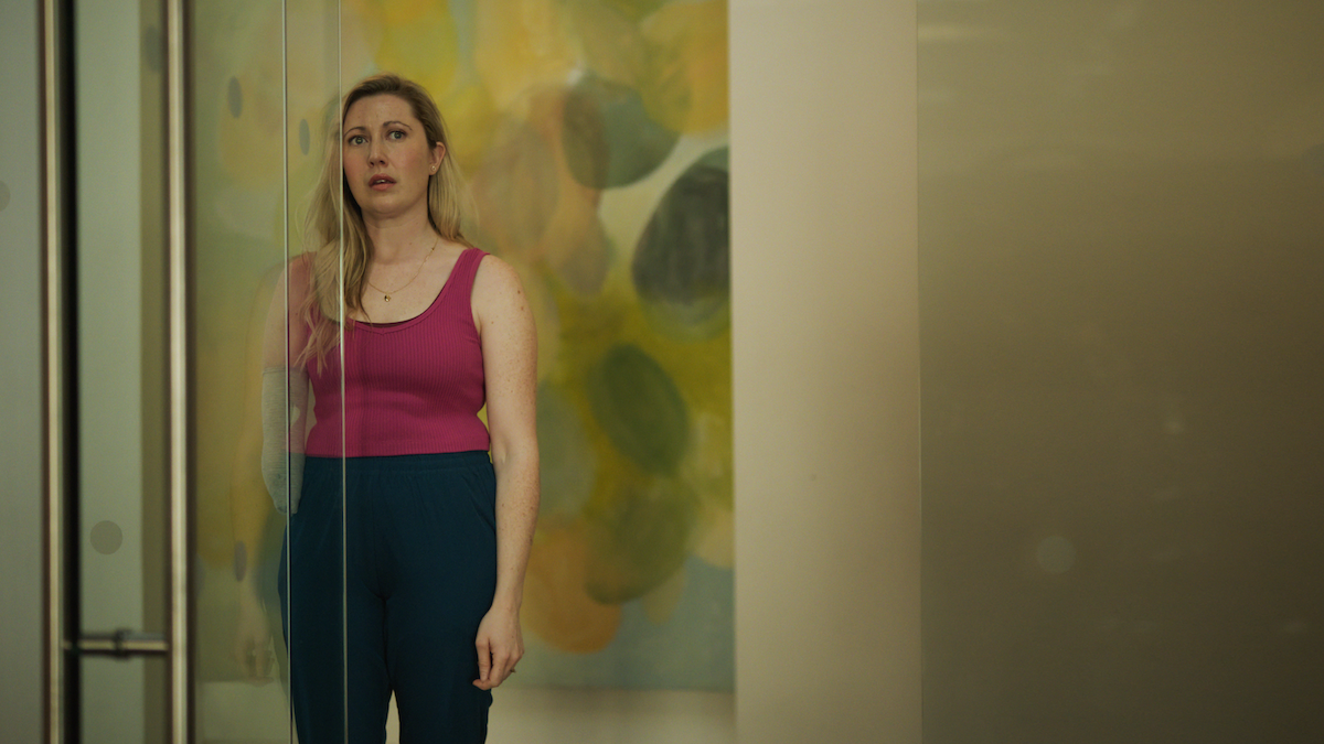A medium shot from the film “The Cockroach” of a woman standing behind a glass door.