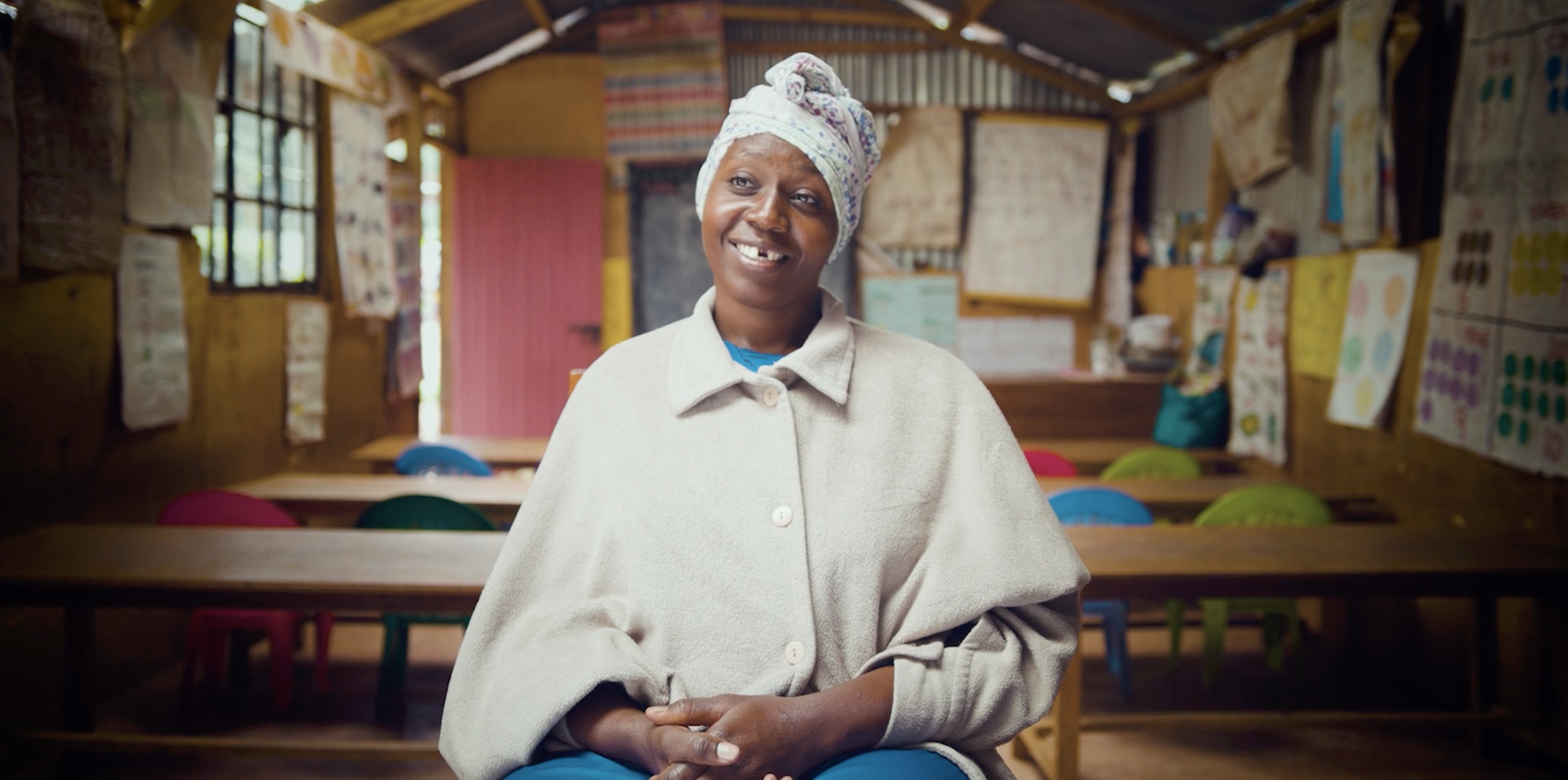 A medium shot from the documentary film “The Curse of Stigma” of a woman sitting in a children’s classroom.