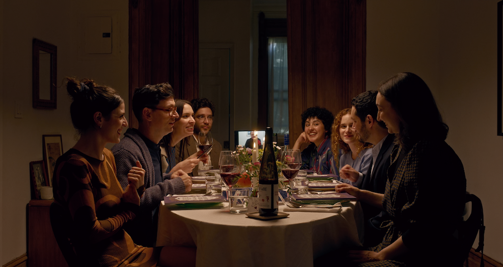A medium shot from the film “Elijah” of a group of friends gathered around a wine and candle-lit dinner.