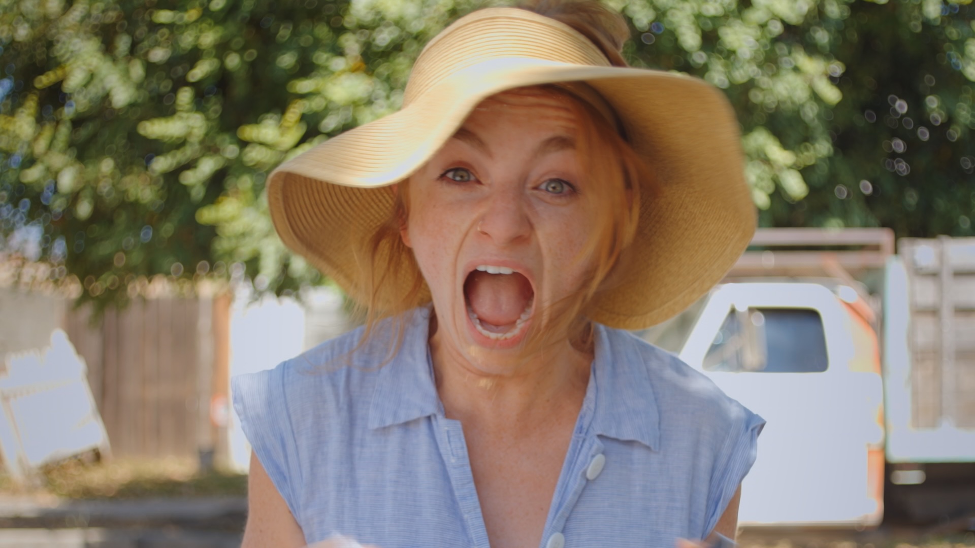 A close-up shot from the film “And Usted Tambien” of a woman wearing a sunhat screaming under the shade of the tree.