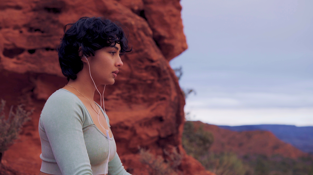 A medium shot from the film “FLOW” of a short-haired woman wearing headphones and staring at the distance.
