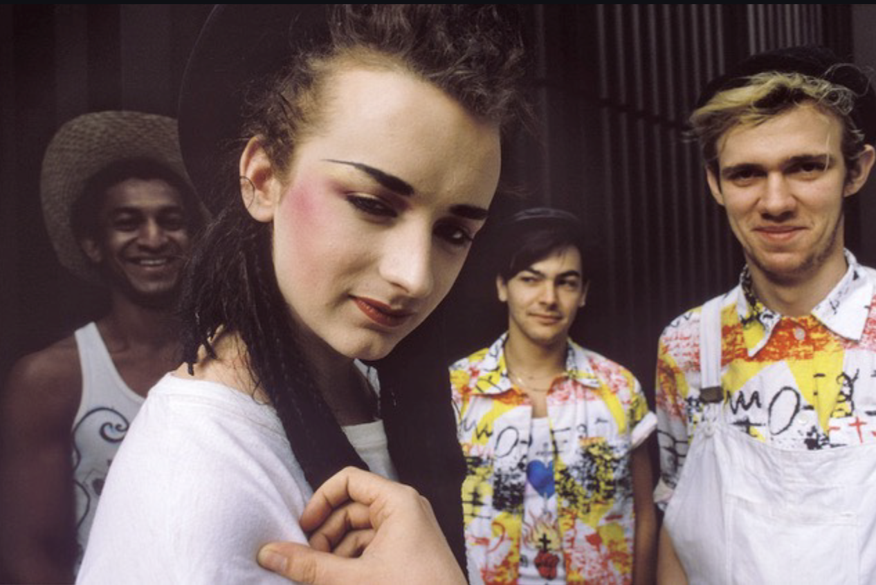 Members of the band Culture Club pose together, with the lead singer in front and bandmates smiling behind.