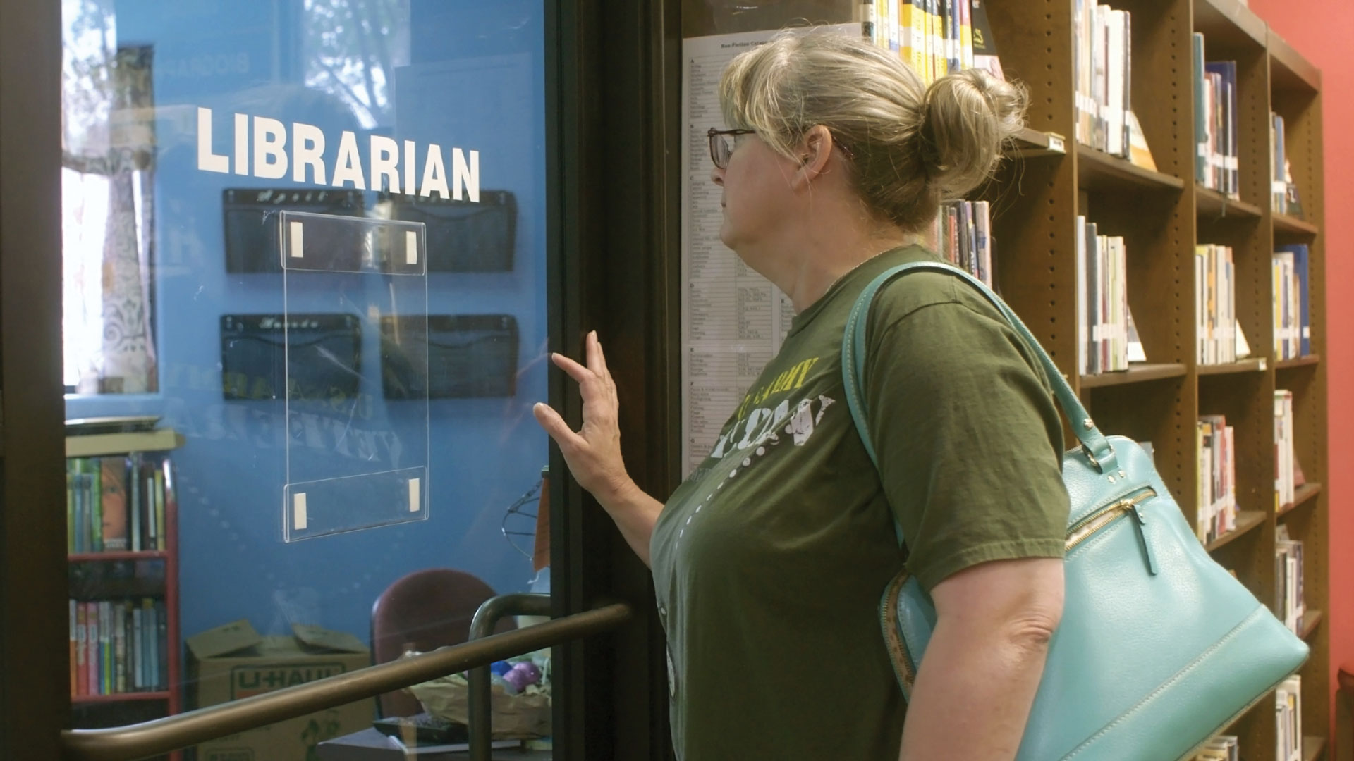 A medium shot from the film “The Librarians” of a woman standing in front of a door that is labeled “LIBRARIAN” and pressing her hand against it.