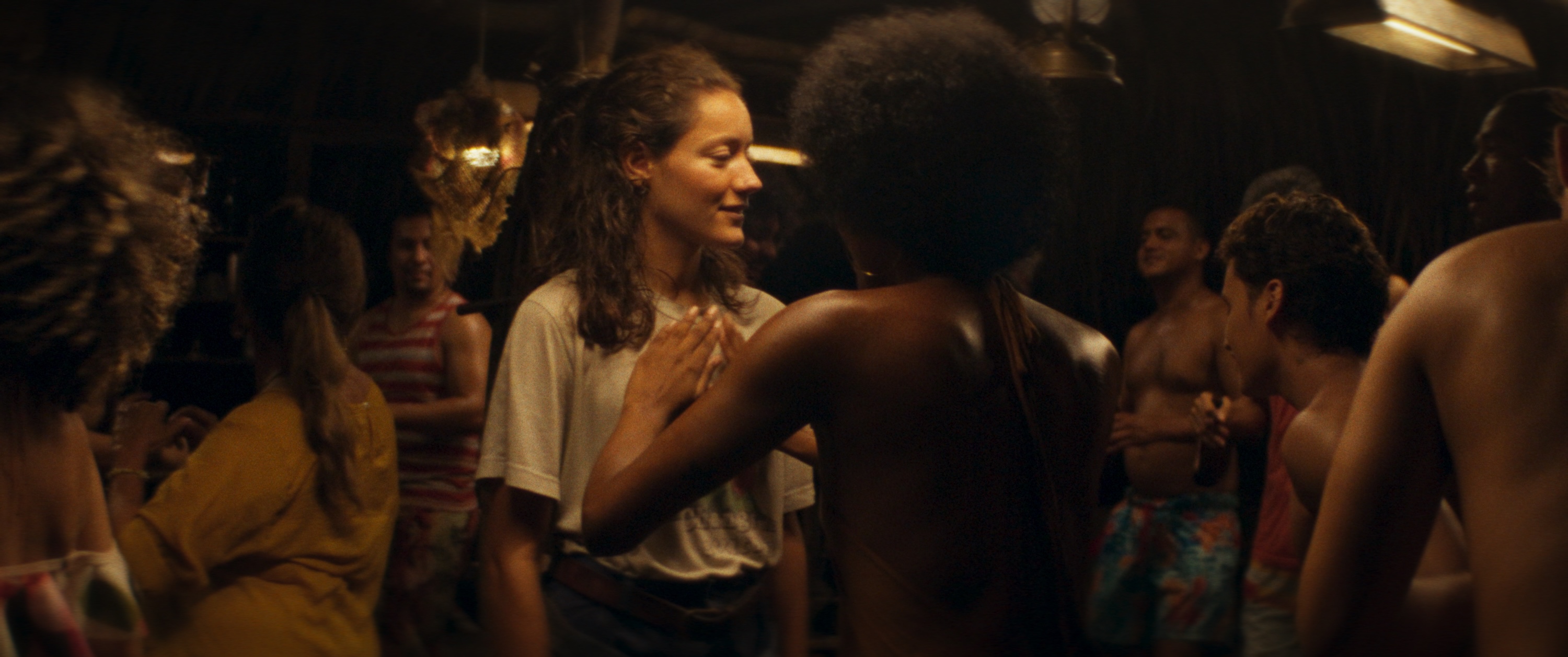 A medium shot from the film “Salsa” of a woman holding her hands up to another woman’s chest. The overhead lights create a warm light in the room.