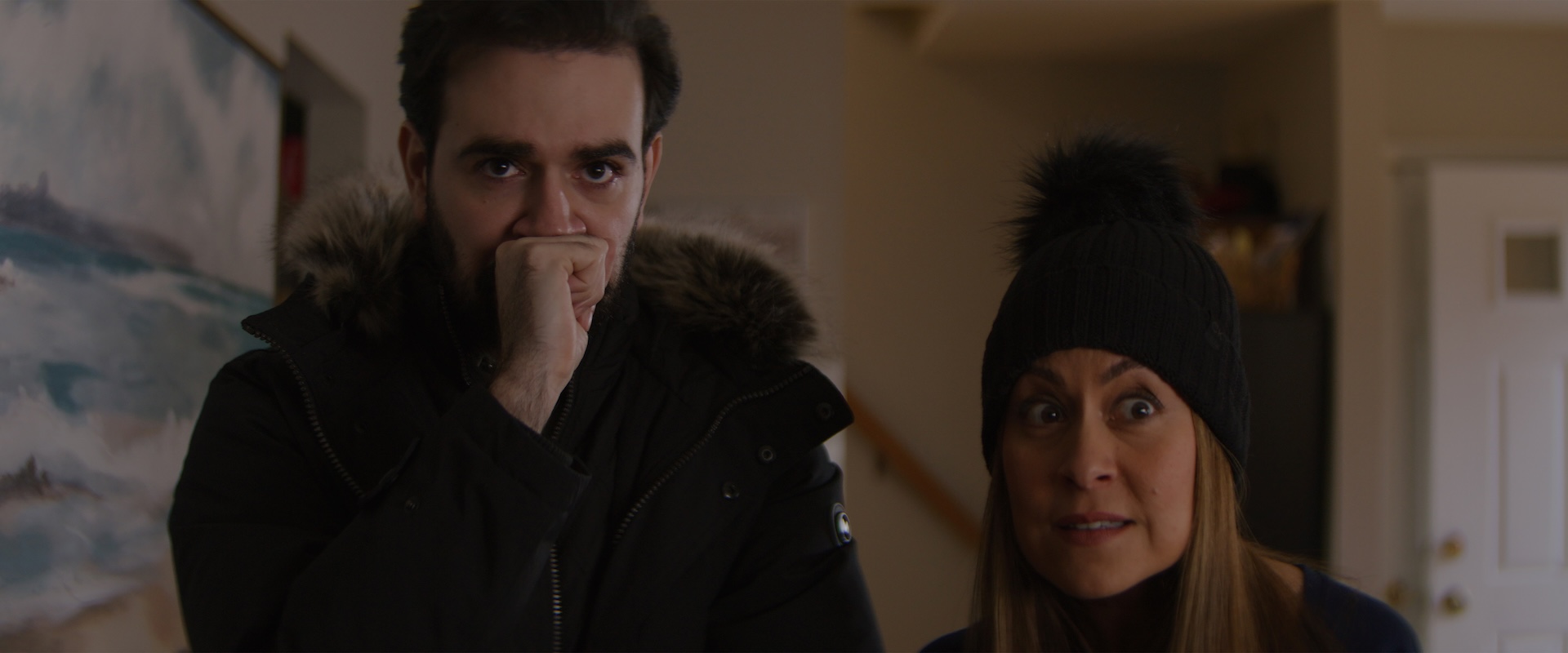 A medium shot from the film “Don’t Bring Empanadas” of a man nervously holding a fist up to his mouth and a woman staring at something askance.