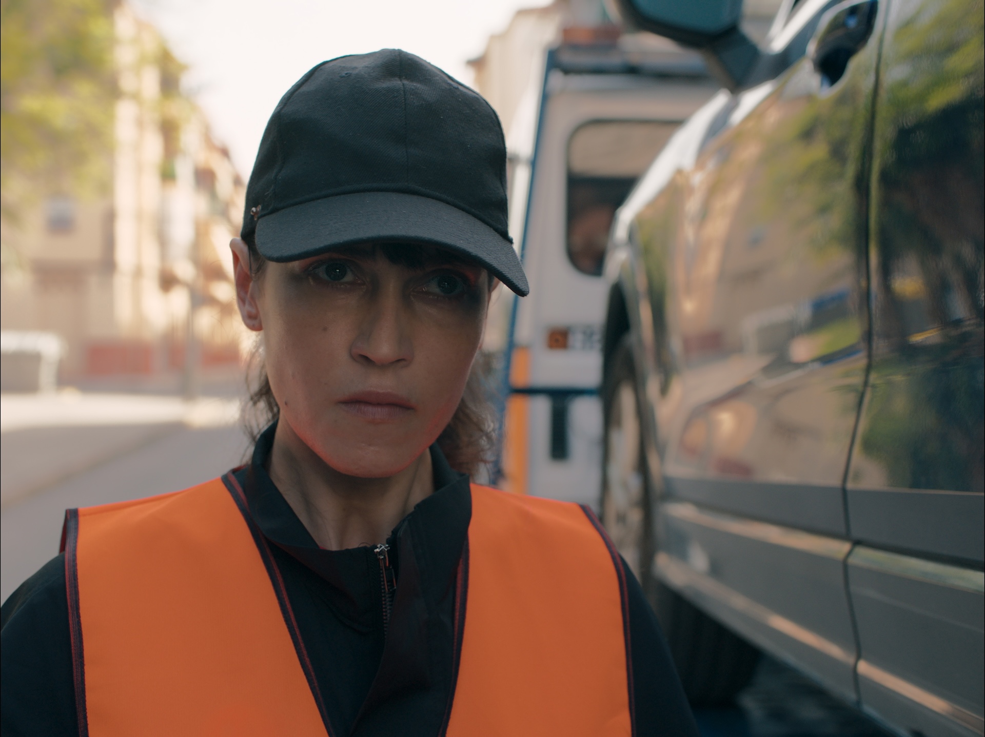 A close-up shot from the film “BERTA” of a female tow truck driver wearing a black cap looking at the distance angrily.