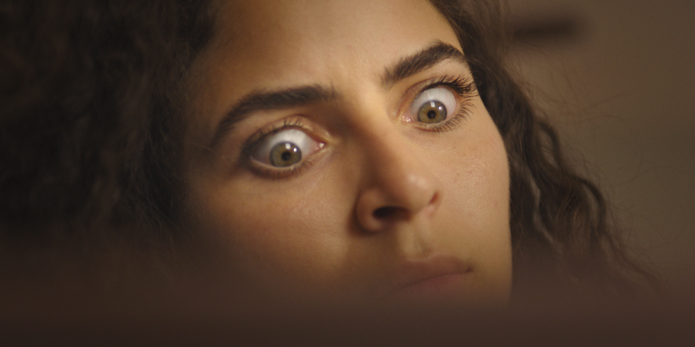 A close up shot from the film “Tacocunr” of a woman widely opening her eyes in shock.