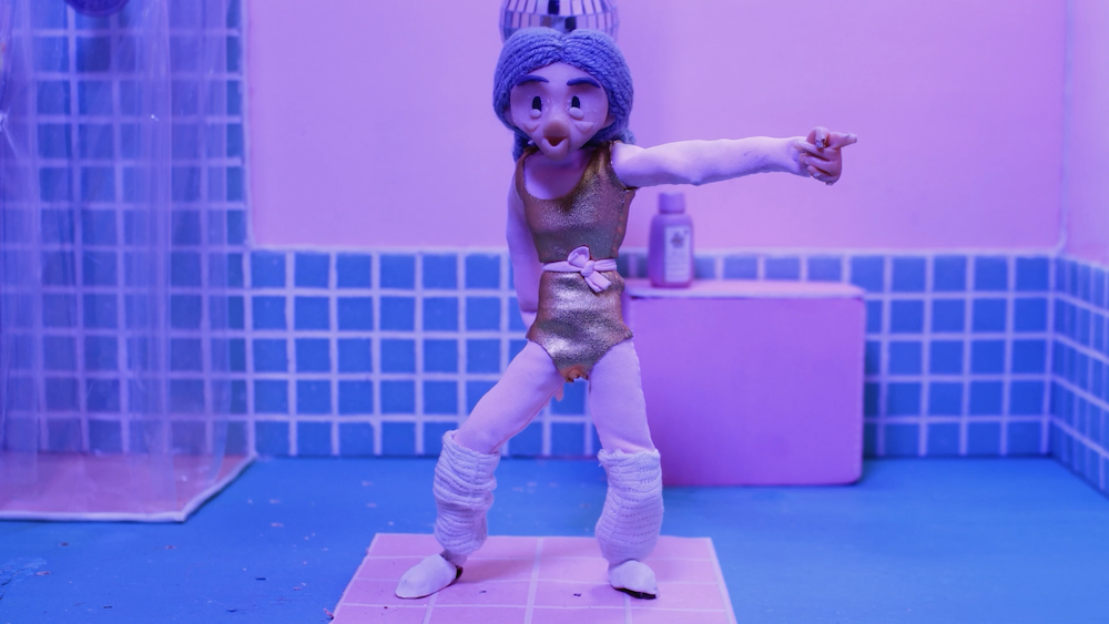 A claymation still from the film “Dance Into the Day” of an aerobics dancer pointing their finger to the right.