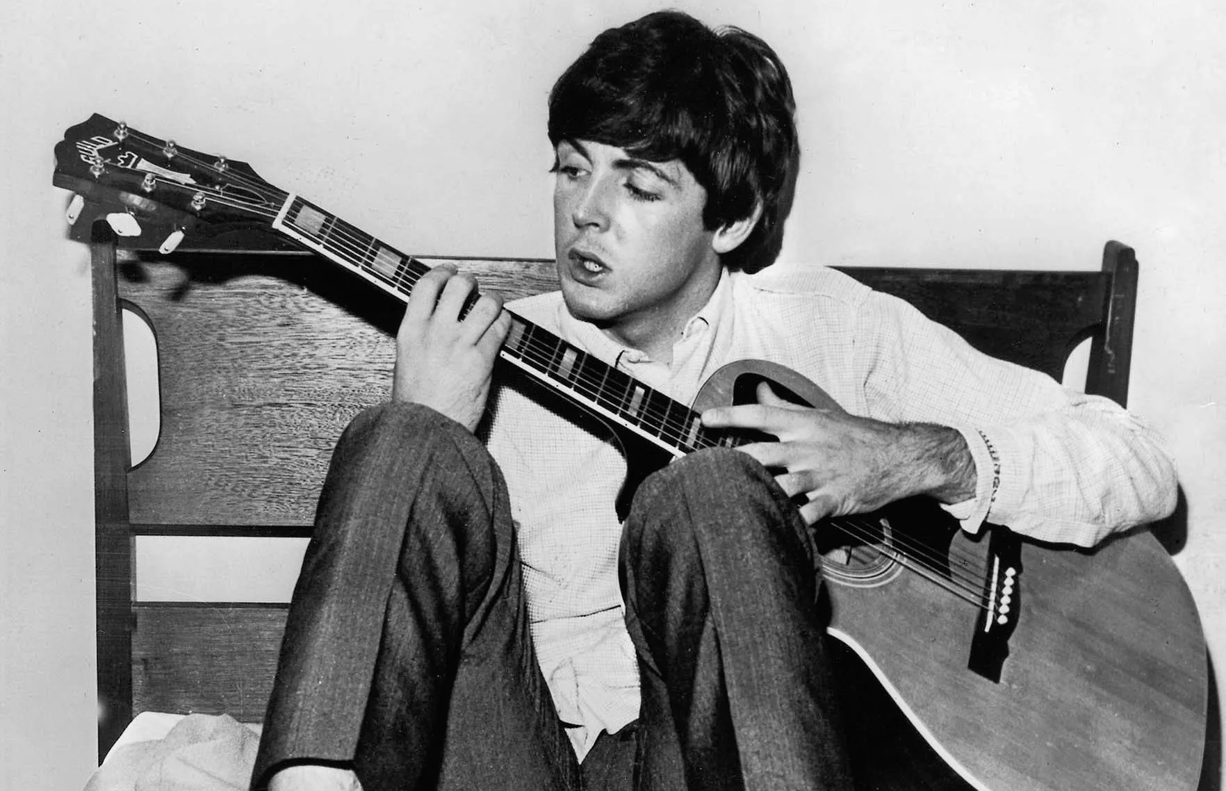 A still from the documentary “Man on the Run” of Paul McCartney sitting on a chair while strumming his guitar.
