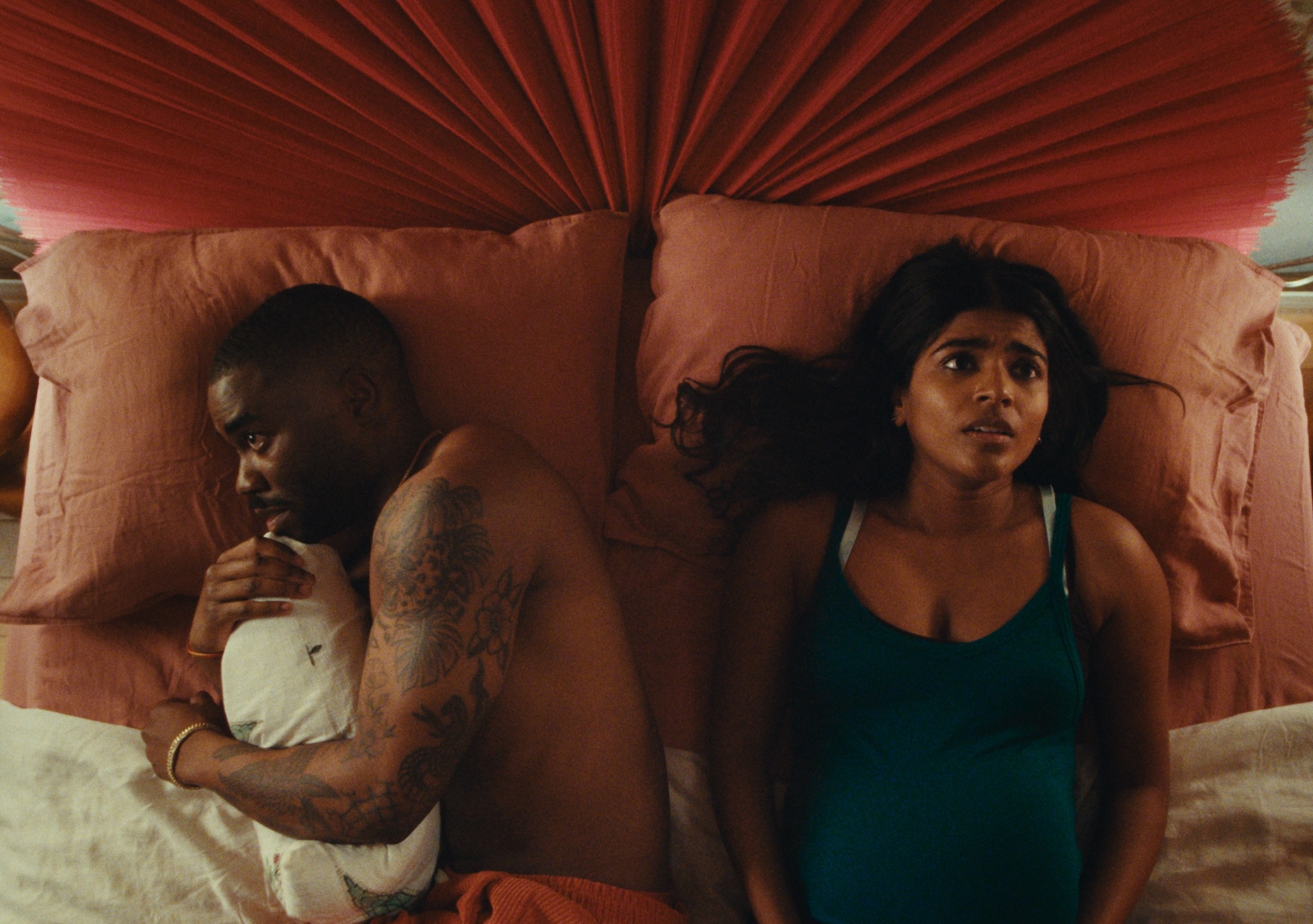 A medium shot from the film “Giving Mom the Talk” of a woman and man laying in bed. The man is laying on his side and the woman is staring at the ceiling, both worried.