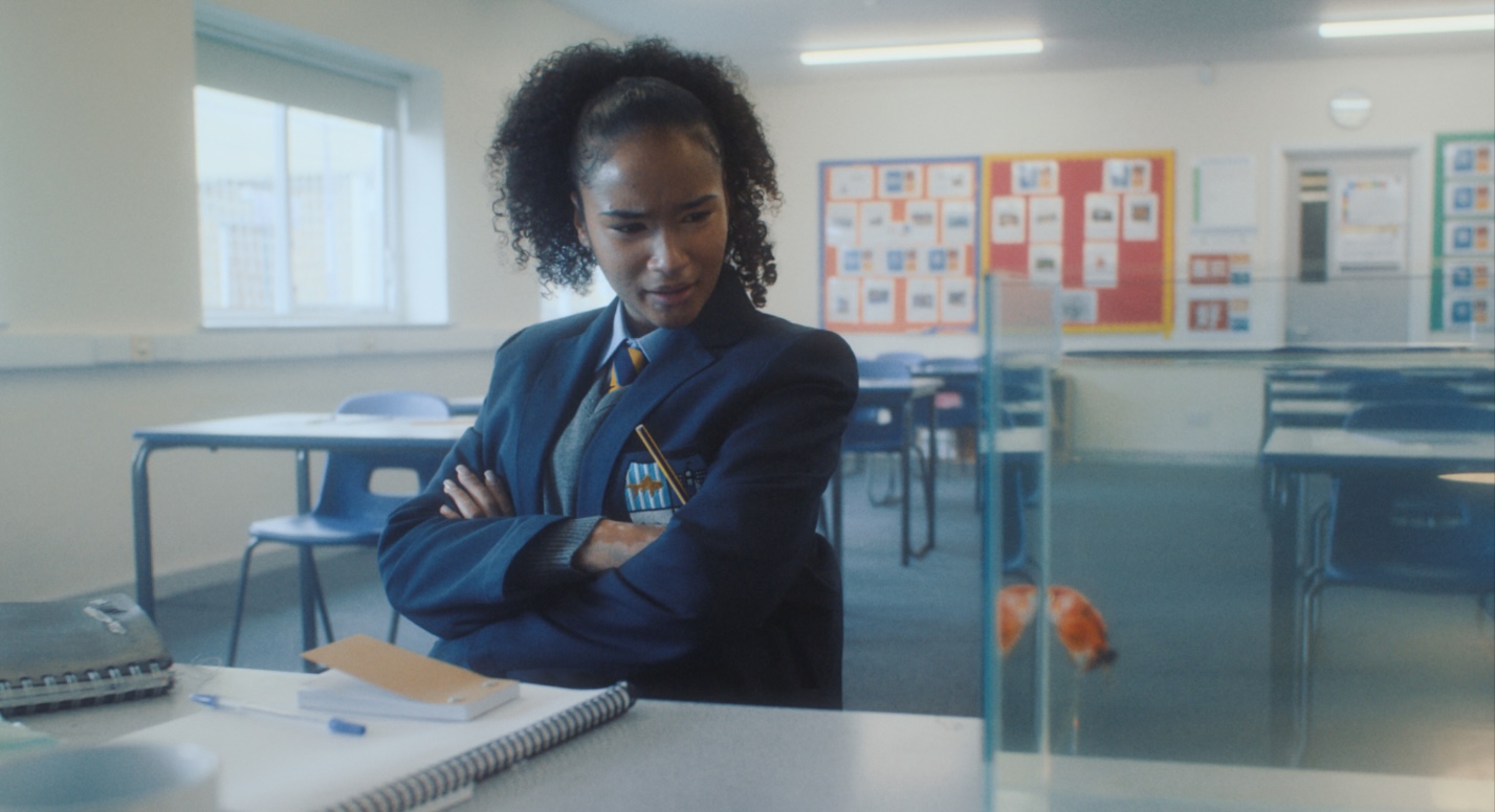 A medium shot from the film “Calico” of a woman studying in a classroom and staring at a goldfish in a clear fish tank.