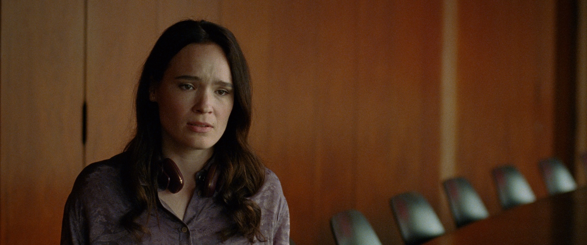 A medium shot from the film “I’m Not a Robot” of a woman with headphones around her neck in a conference room.