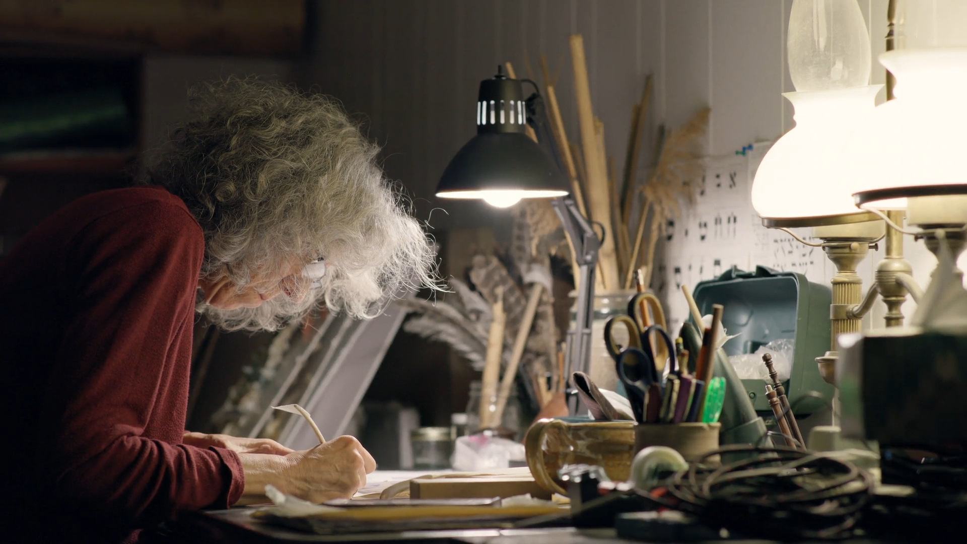 A close-up shot shows a person's hand using a traditional quill to carefully scribe Hebrew letters onto a textured parchment scroll.