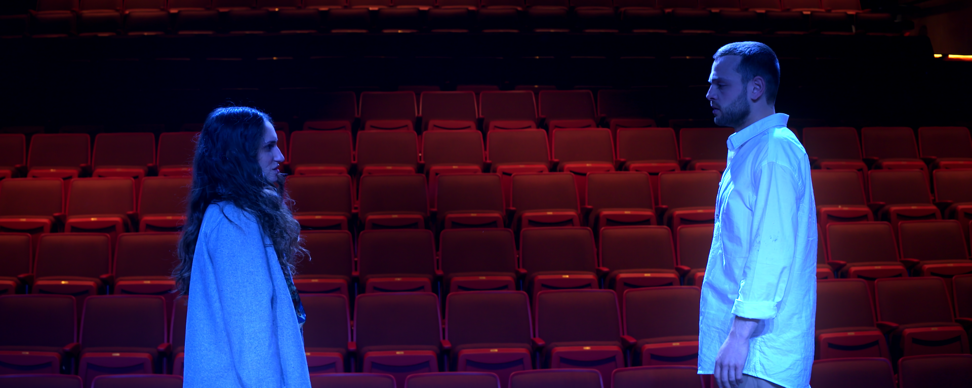 A medium shot of a man and a woman standing facing each other in front of an empty theater.